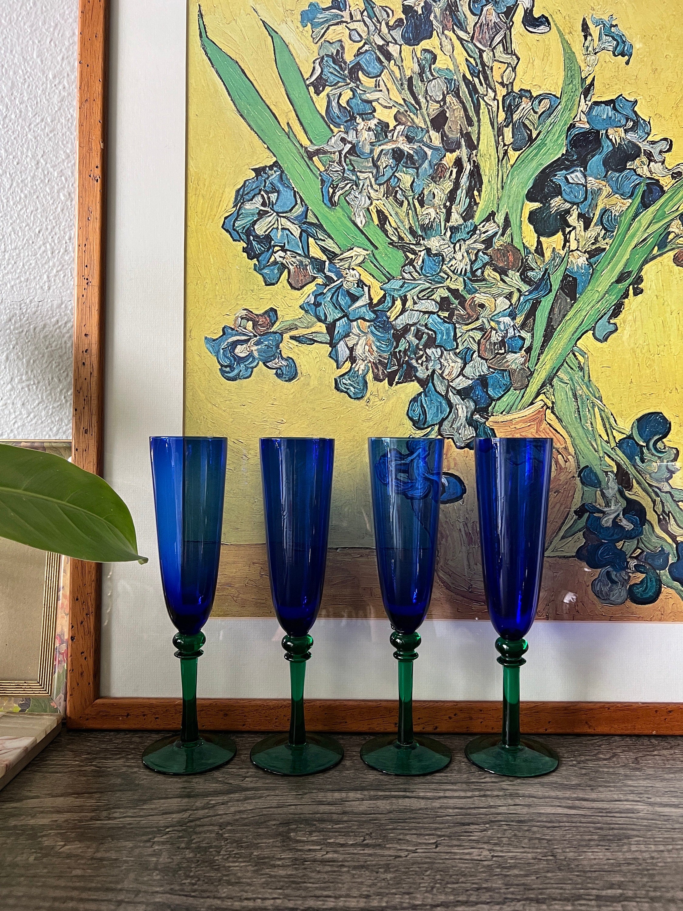 Four blue and green tall glasses in front of a Van Gogh painting of flowers.
